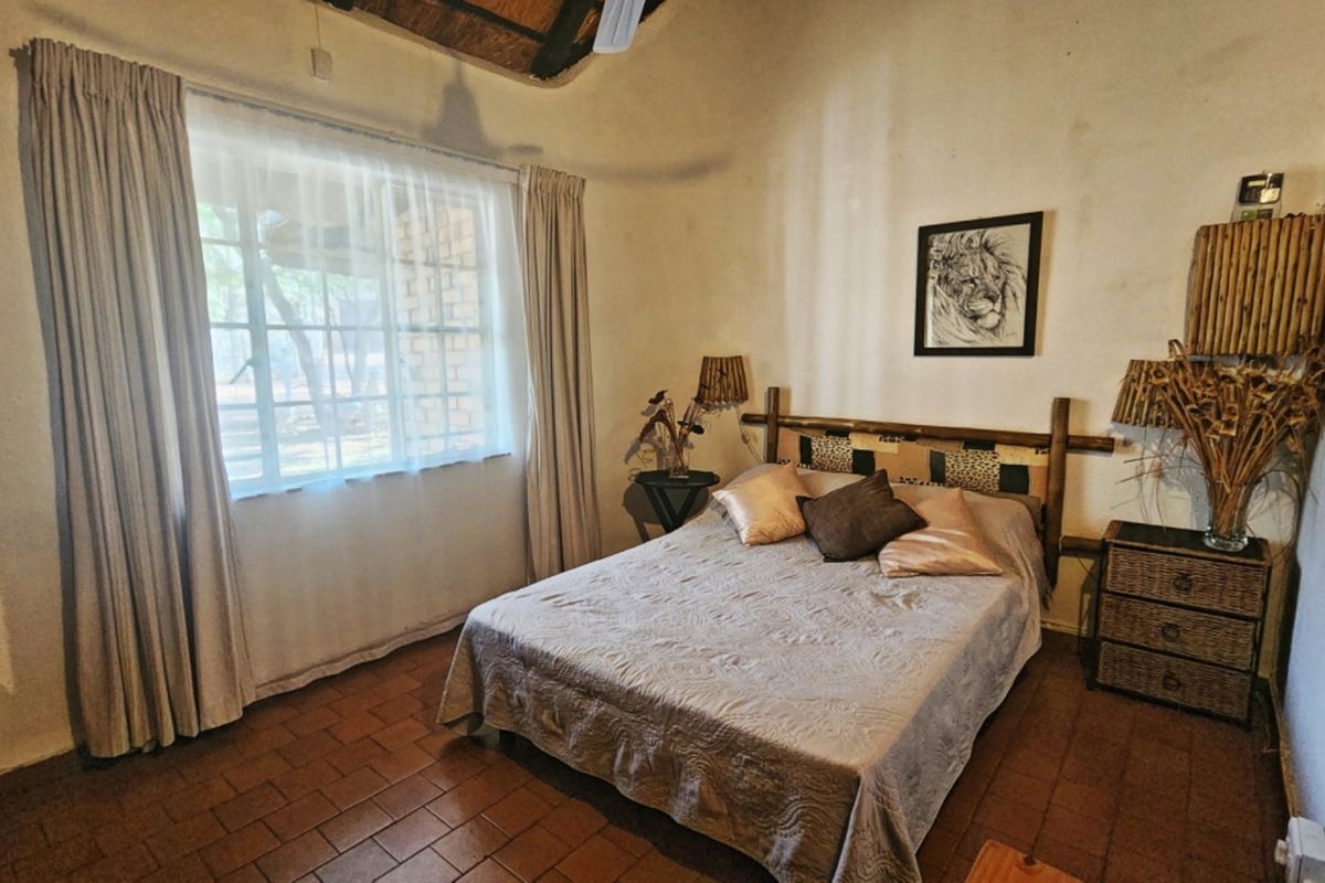 A rustic bedroom featuring exposed timber ceiling beams, a thatched roof, and terracotta floor tiles, offering a cozy, traditional atmosphere.