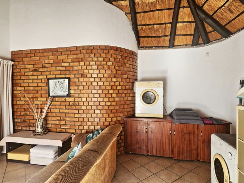 Living area featuring a unique curved exposed brick wall, traditional thatched ceiling, and tiled flooring with integrated storage cabinetry.