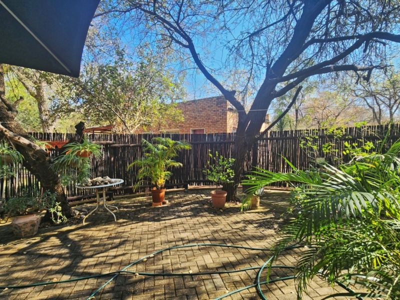 A private garden area featuring paved flooring, mature trees, and traditional timber pole fencing, offering a quiet outdoor space.