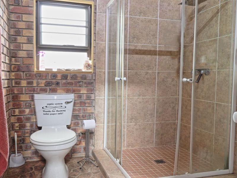 A functional bathroom featuring exposed brick walls, a glass-enclosed shower, a pedestal basin, and a toilet, showcasing a rustic, dated aesthetic.