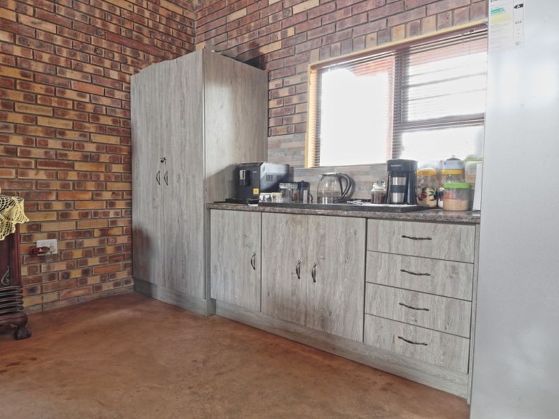 A functional scullery area featuring exposed brick walls, modern laminate cabinetry, stone-look countertops, and durable concrete flooring.