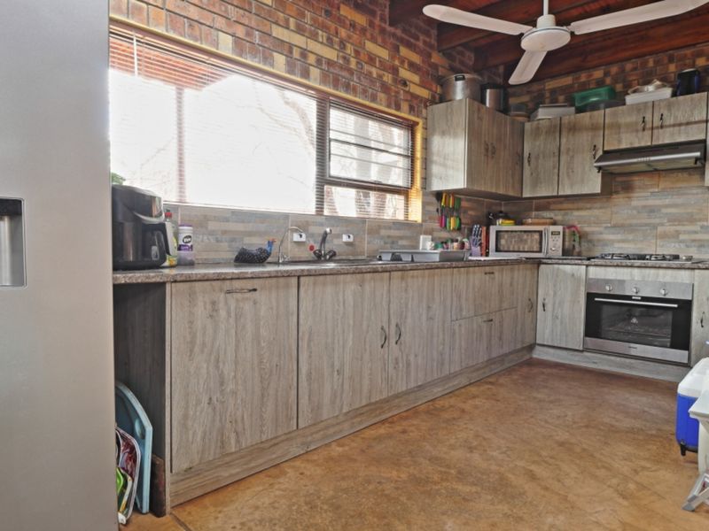 Functional kitchen featuring wood-look laminate cabinetry, granite countertops, built-in oven and hob, exposed brick walls, and timber ceiling beams.