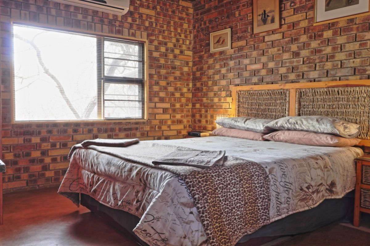 A bedroom featuring rustic exposed brick walls, an air conditioning unit, and a large window with security bars.