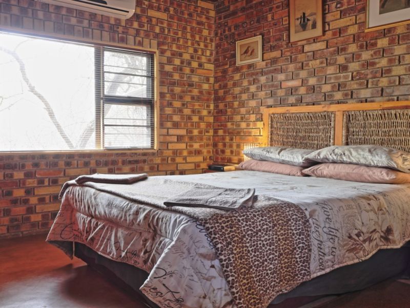 A bedroom featuring rustic exposed brick walls, an air conditioning unit, and a large window with security bars.