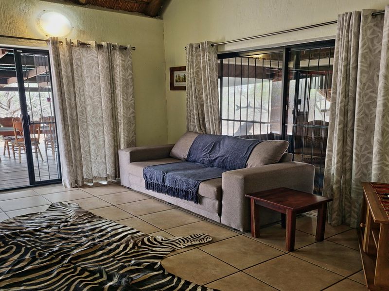 Living room featuring tiled floors, high thatch ceiling, and large sliding glass doors providing direct access to an outdoor patio area.