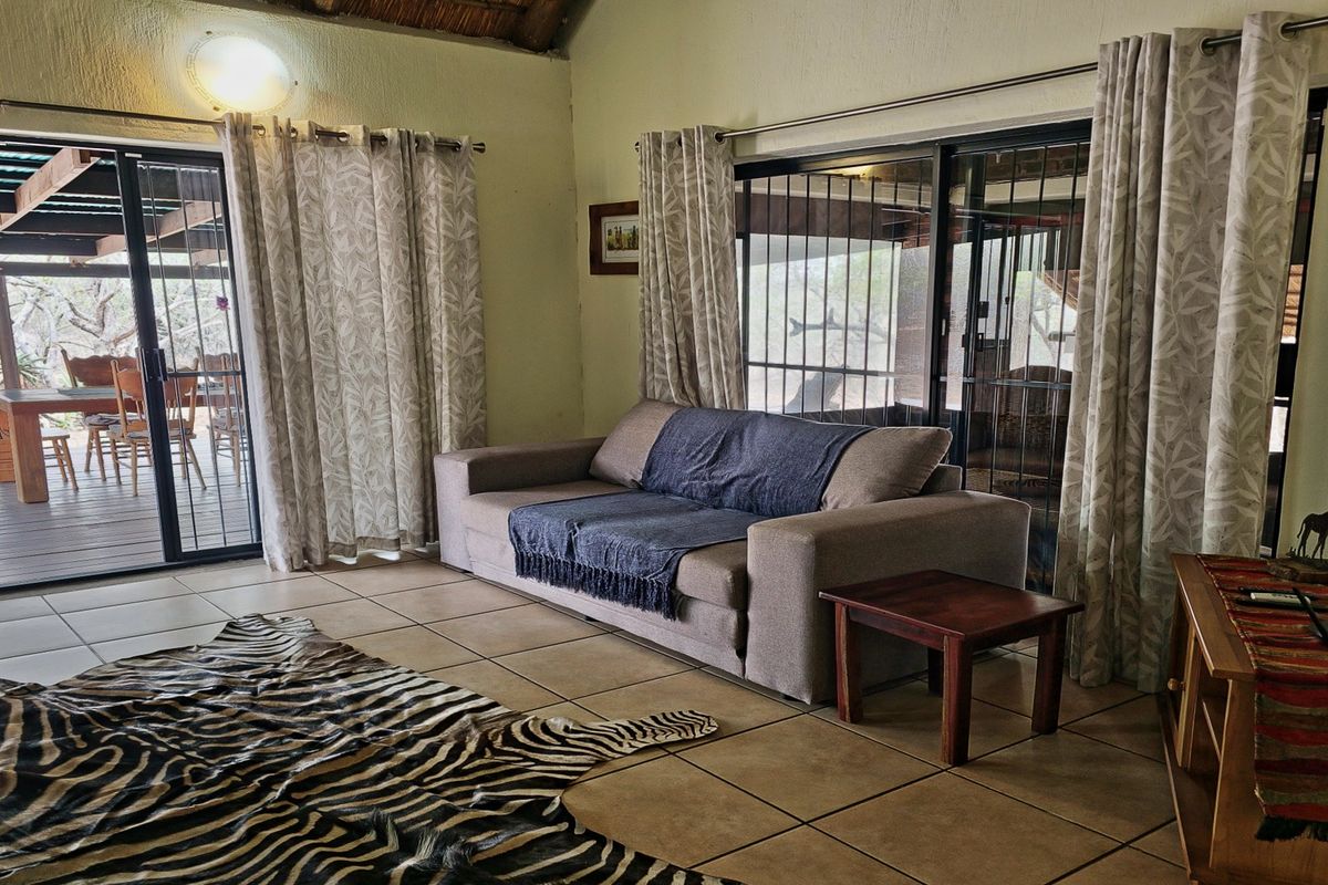 Living room featuring tiled floors, high thatch ceiling, and large sliding glass doors providing direct access to an outdoor patio area.