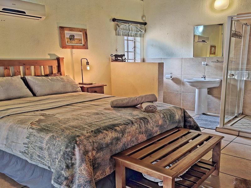 A bedroom featuring an open-plan layout with an integrated en-suite bathroom, including a pedestal basin and a glass-enclosed shower.