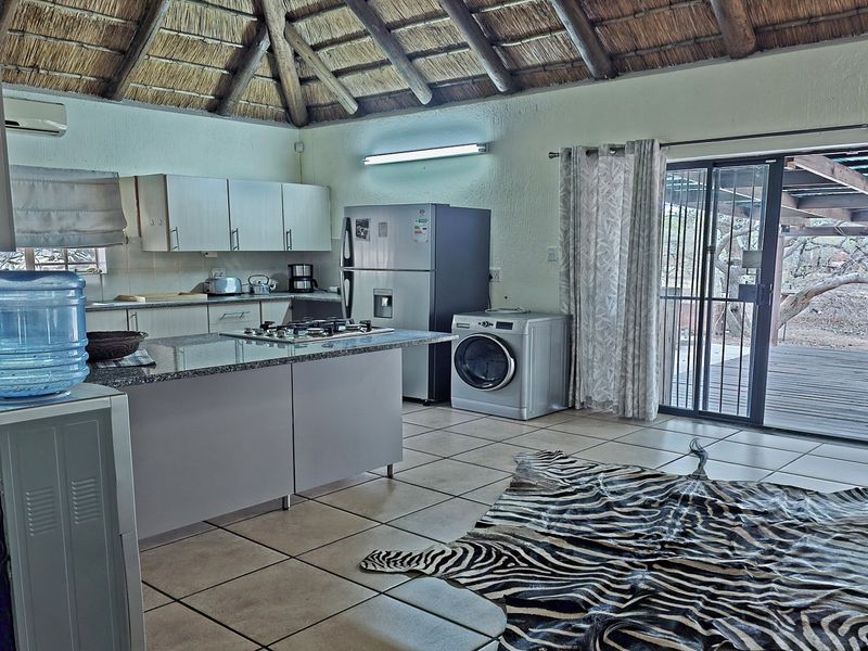 Open-plan kitchen and living area featuring a traditional thatched roof with exposed rafters, tiled flooring, and direct access to an outdoor deck.