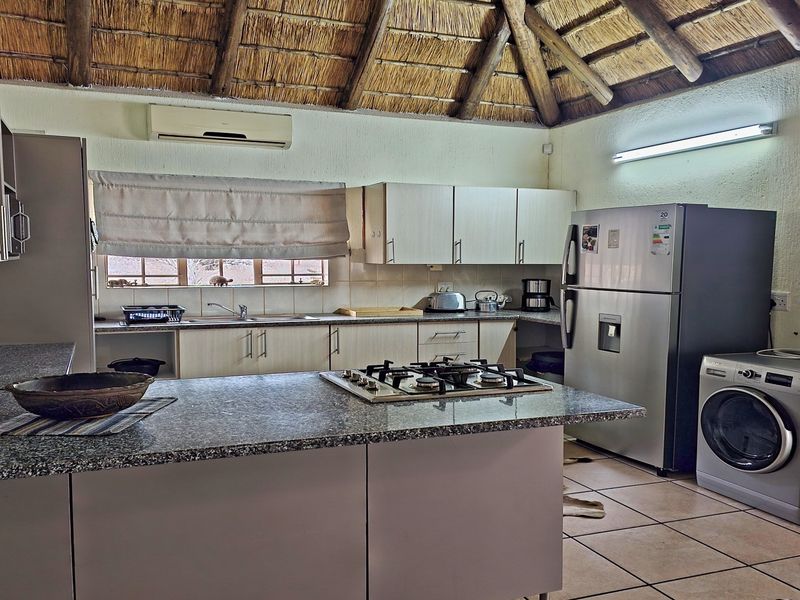 Spacious kitchen featuring granite countertops, a gas hob, built-in cabinetry, and a unique vaulted thatch ceiling with exposed timber beams.