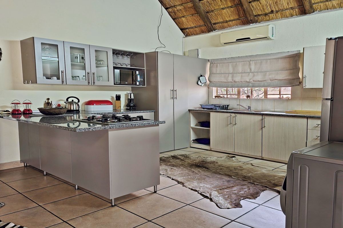 A functional kitchen featuring light-toned cabinetry, granite countertops, a gas hob, and a distinctive vaulted thatch ceiling with exposed beams.