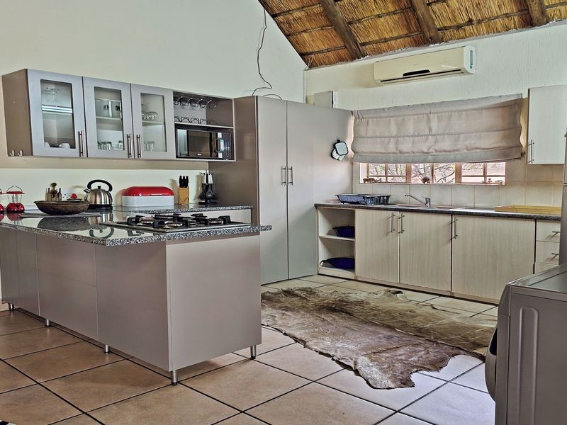 A functional kitchen featuring light-toned cabinetry, granite countertops, a gas hob, and a distinctive vaulted thatch ceiling with exposed beams.