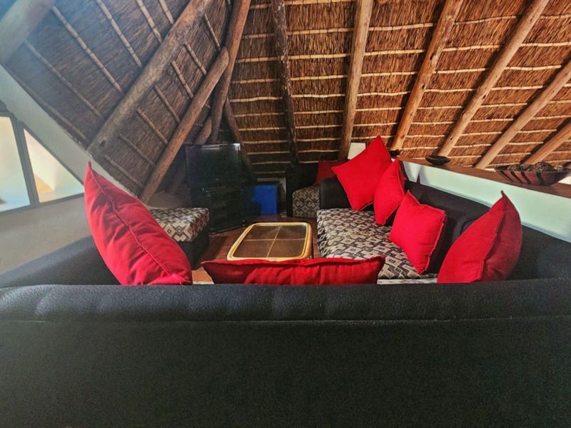 A cozy mezzanine living area featuring a traditional exposed thatch roof and timber rafters, creating a unique rustic atmosphere.