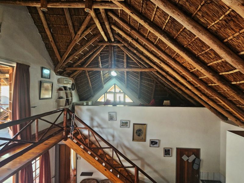 Spacious living area featuring a high-pitched thatched roof with exposed timber rafters, a wooden staircase, and a unique triangular gable window.