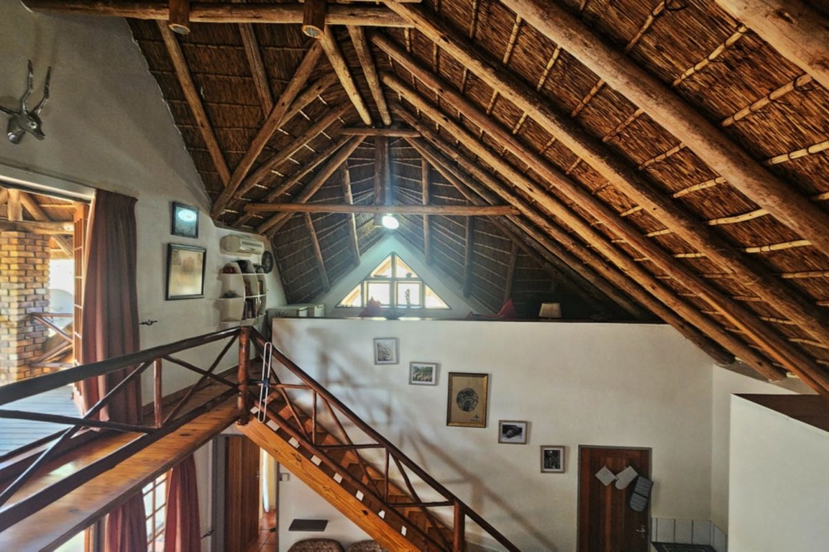 Spacious living area featuring a high-pitched thatched roof with exposed timber rafters, a wooden staircase, and a unique triangular gable window.