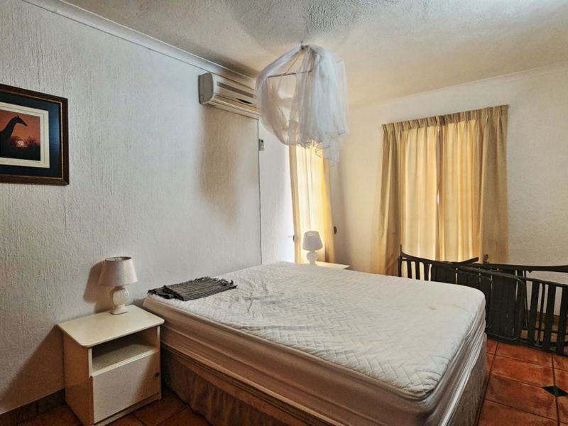A functional bedroom featuring tiled flooring and a wall-mounted air conditioning unit, providing a comfortable space with basic fixed finishes.