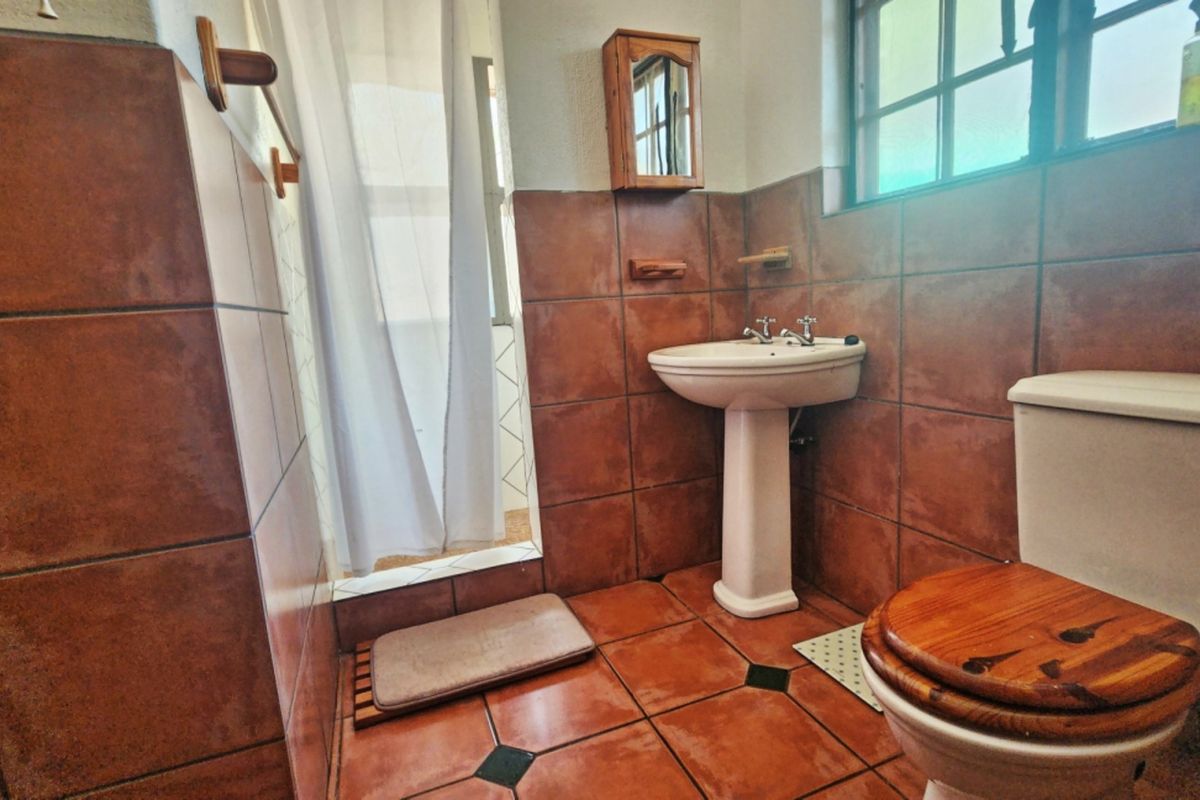 A compact bathroom featuring a pedestal basin, toilet, and shower area with dated terracotta-style wall and floor tiling.