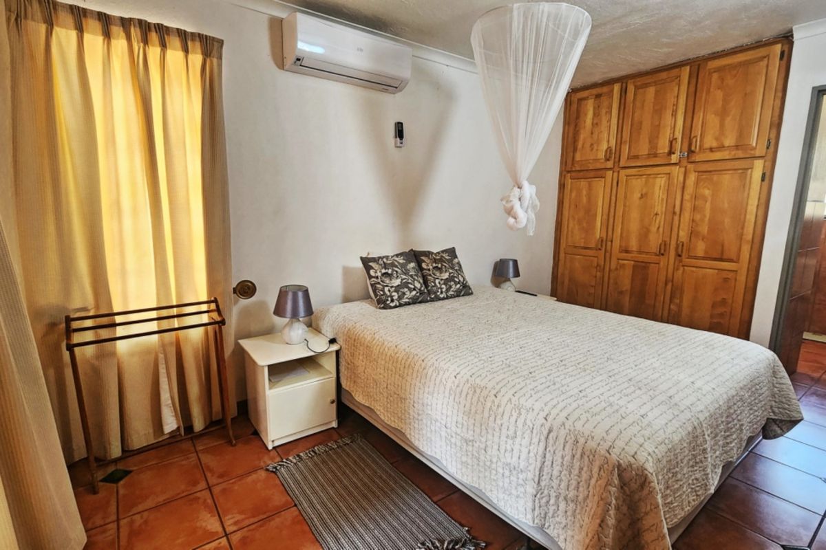 A bedroom featuring built-in wooden cupboards, tiled flooring, and a wall-mounted air conditioning unit, with an adjoining bathroom visible.