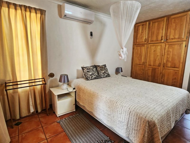 A bedroom featuring built-in wooden cupboards, tiled flooring, and a wall-mounted air conditioning unit, with an adjoining bathroom visible.