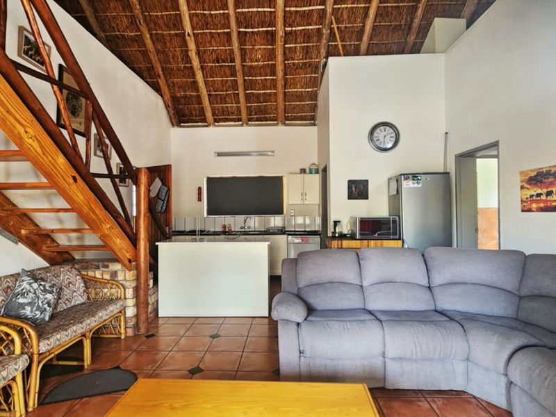 Open plan living area featuring a high thatched ceiling with exposed timber rafters, tiled flooring, and an integrated kitchen space with a wooden staircase.