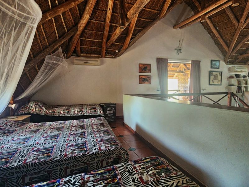 Spacious loft-style bedroom featuring a high exposed timber thatch roof, tiled flooring, and a private balcony access point.