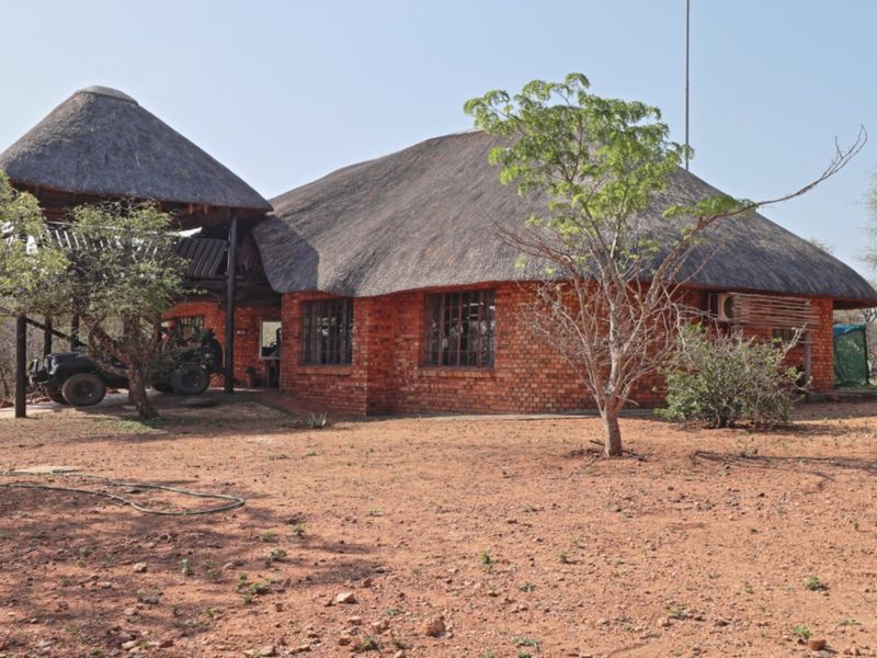 A rustic, single-story house featuring traditional thatch roofing and exposed brick exterior walls, set within a natural bushveld landscape.