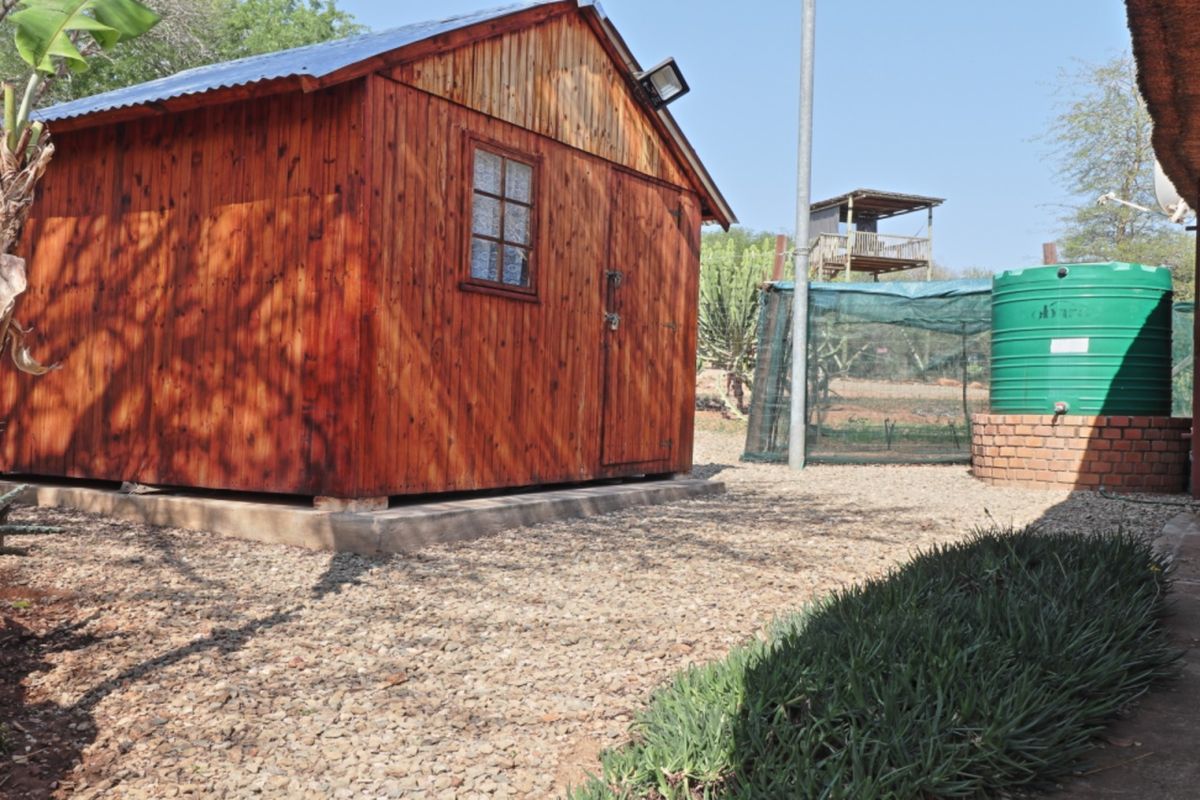 Rear garden area featuring a timber cabin, a green water storage tank on a brick base, and gravel landscaping.
