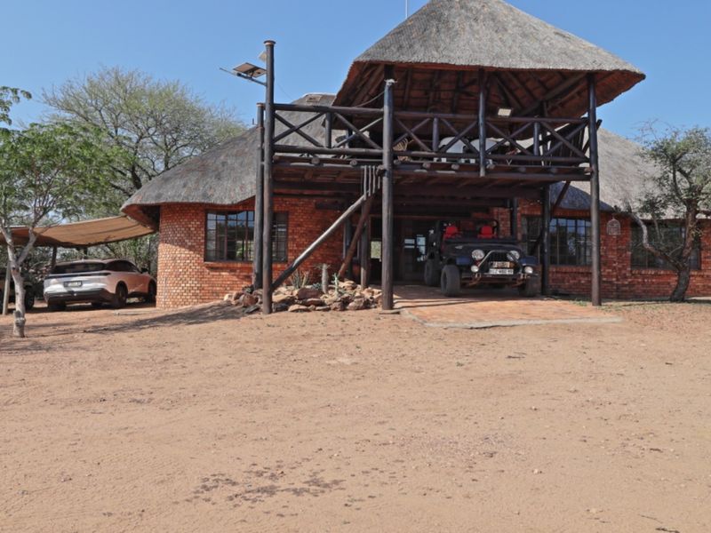 Front exterior view of a rustic house featuring a thatched roof, exposed brick walls, and a raised timber balcony structure.