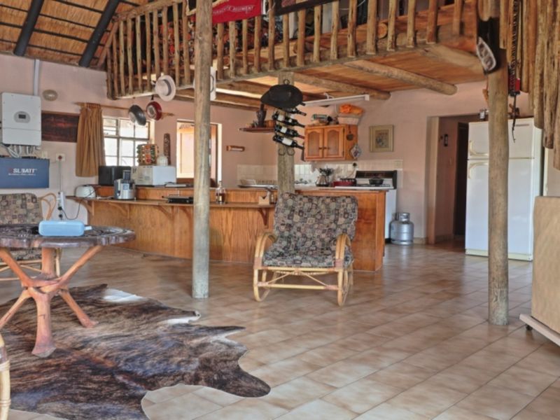 Spacious open-plan living area featuring a rustic thatched roof, exposed timber beams, a mezzanine loft, and a functional kitchen with a breakfast bar.