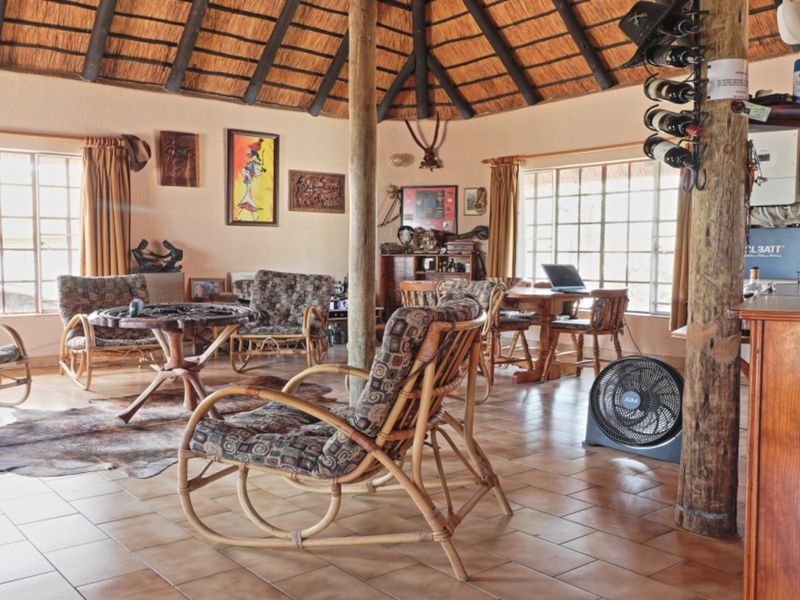 Spacious living area featuring a traditional thatched roof, exposed timber support columns, and ceramic tile flooring with large windows providing natural light.