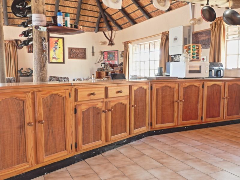 A rustic kitchen featuring wooden cabinetry, tiled flooring, and a traditional thatch roof with exposed timber support beams.