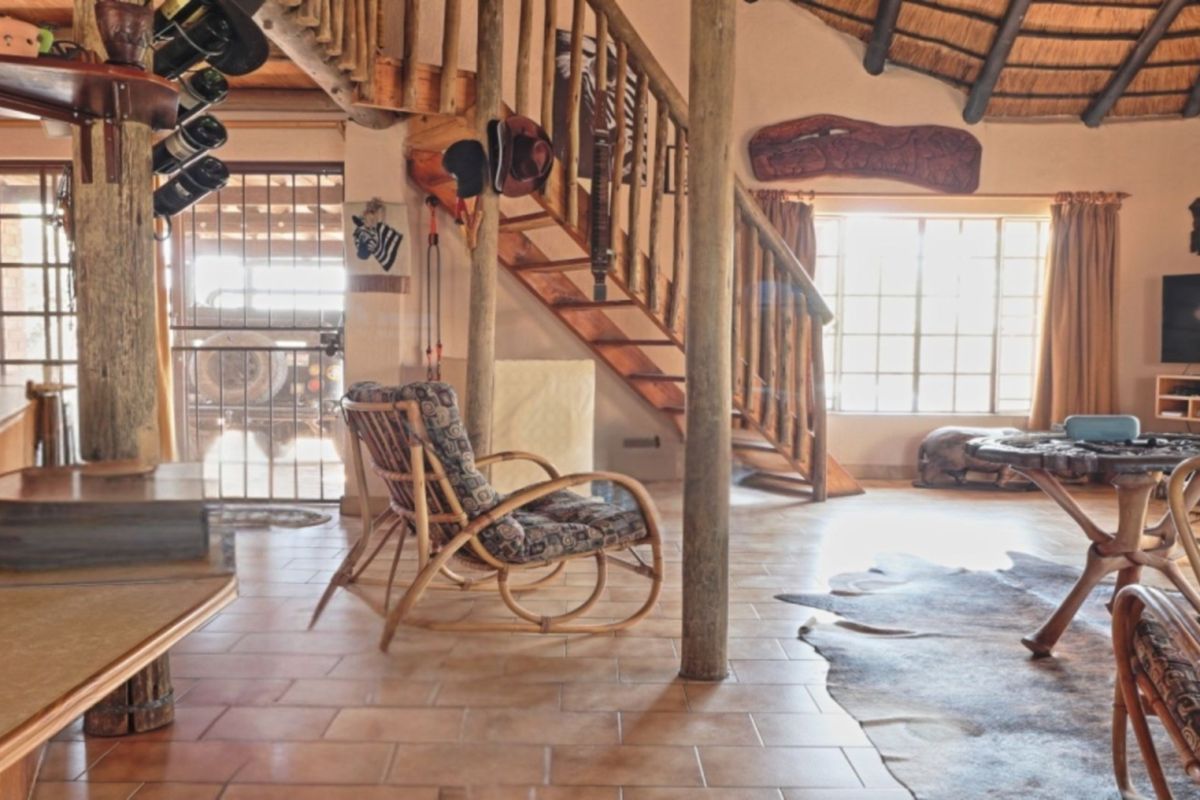 Rustic living area featuring a wooden staircase, exposed timber support poles, and a traditional thatched roof ceiling with tiled flooring.