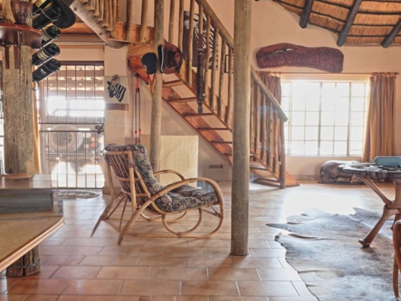 Rustic living area featuring a wooden staircase, exposed timber support poles, and a traditional thatched roof ceiling with tiled flooring.