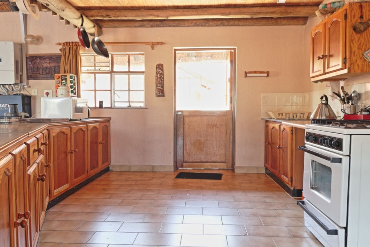 Rustic kitchen featuring timber cabinetry, exposed ceiling beams, tiled flooring, and a stable door leading to the exterior.