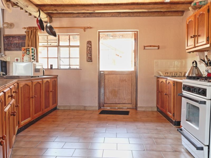 Rustic kitchen featuring timber cabinetry, exposed ceiling beams, tiled flooring, and a stable door leading to the exterior.