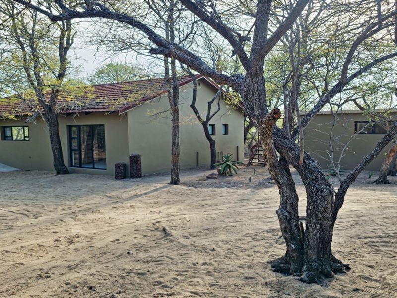 Rear view of a single-story house featuring a tiled roof, neutral exterior walls, and large sliding glass doors set within a natural, sandy landscape.