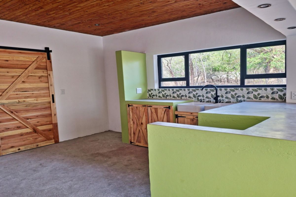A modern kitchen featuring a timber ceiling, concrete countertops, double basin sink, and a rustic barn-style sliding door, offering a unique aesthetic.