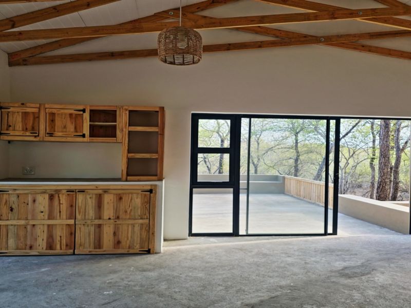 Open plan living area featuring exposed timber roof trusses, concrete flooring, custom wooden cabinetry, and large sliding doors opening to an outdoor patio.