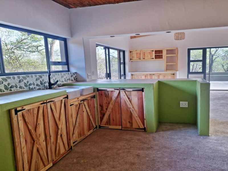 Open-plan kitchen featuring custom timber cabinetry, concrete countertops, and a double farmhouse sink, with direct access to an outdoor patio area.
