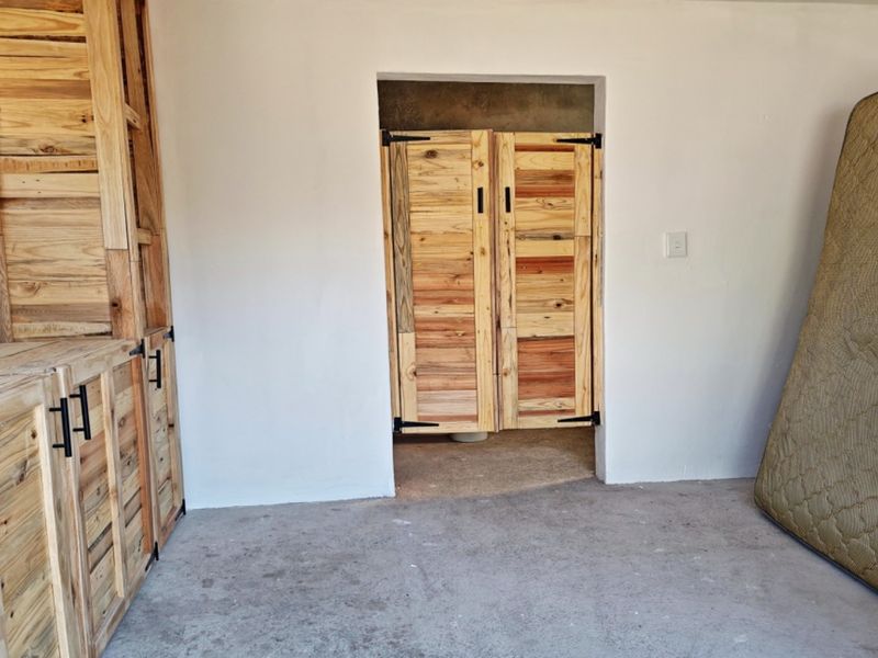 A functional garage space featuring built-in wooden cabinetry, double swing doors, and concrete flooring, offering potential for storage or workshop use.