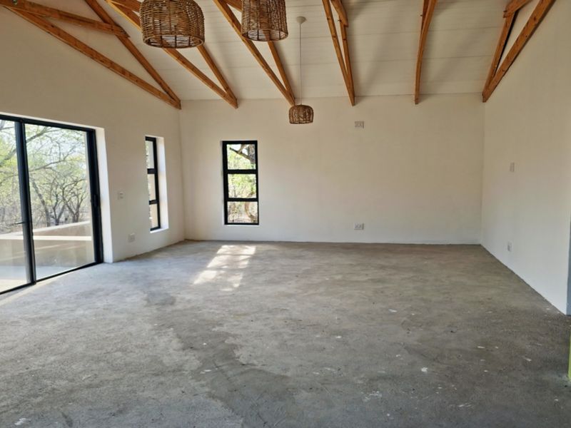 Spacious open-plan living area featuring a vaulted ceiling with exposed timber trusses, large sliding glass doors, and unfinished concrete flooring.