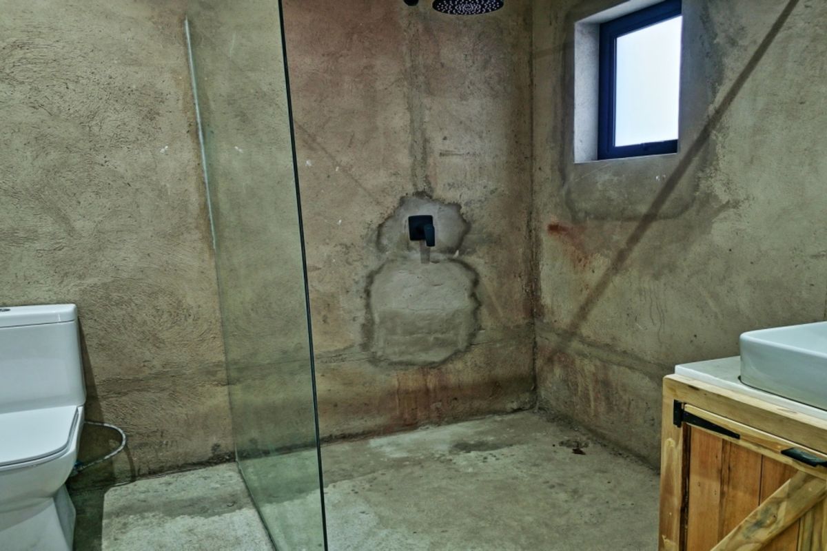 Bathroom featuring a walk-in shower with glass screen, vessel sink on a wooden vanity, and unfinished concrete wall finishes.