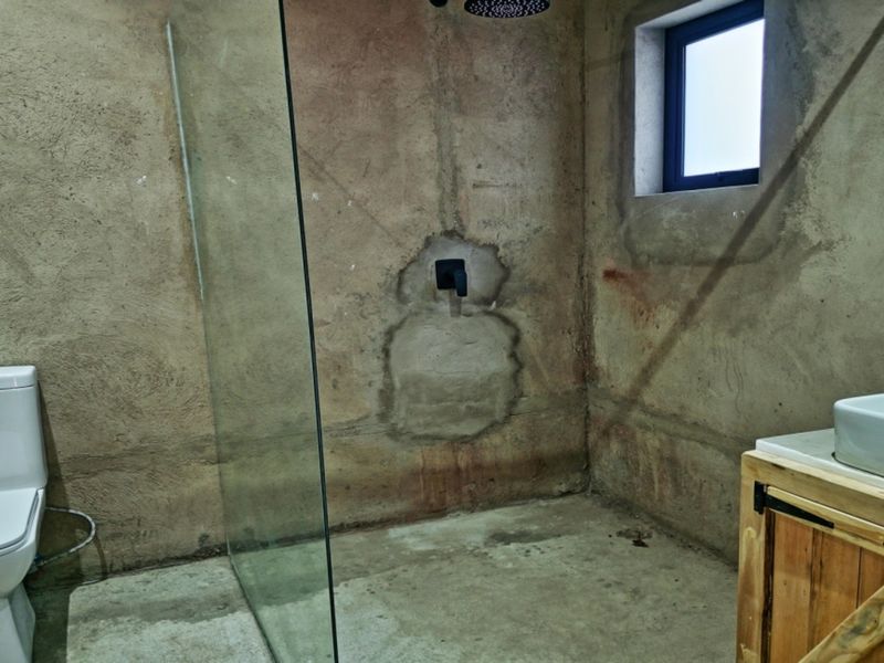 Bathroom featuring a walk-in shower with glass screen, vessel sink on a wooden vanity, and unfinished concrete wall finishes.