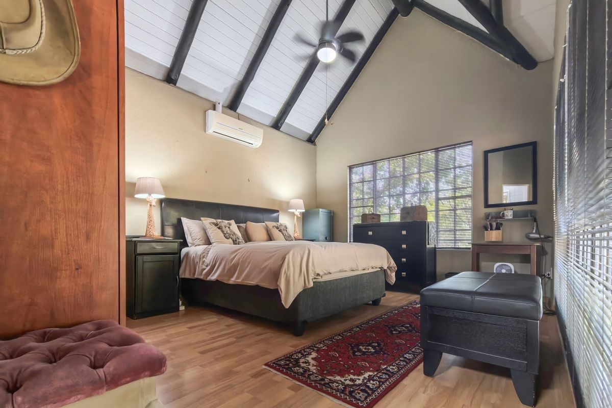 Spacious bedroom featuring a high vaulted ceiling with exposed timber beams, laminate flooring, and a wall-mounted air conditioning unit.