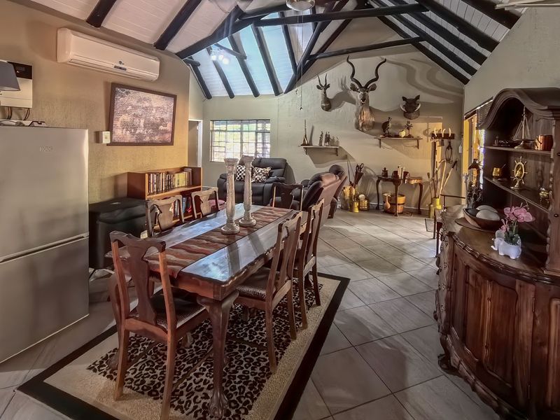 Spacious open-plan living and dining area featuring a high vaulted ceiling with exposed timber beams, tiled flooring, and a wall-mounted air conditioning unit.
