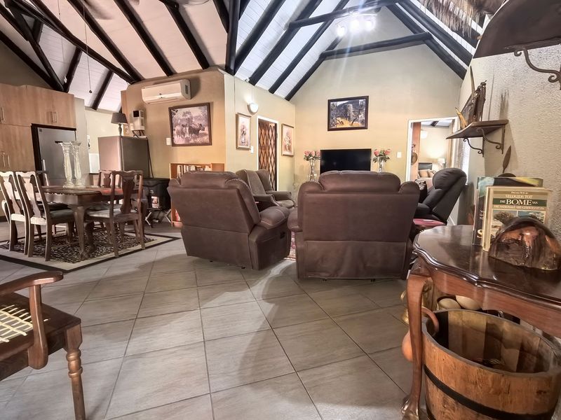 Spacious open-plan living and dining area featuring a high vaulted ceiling with exposed timber beams and neutral tiled flooring throughout.
