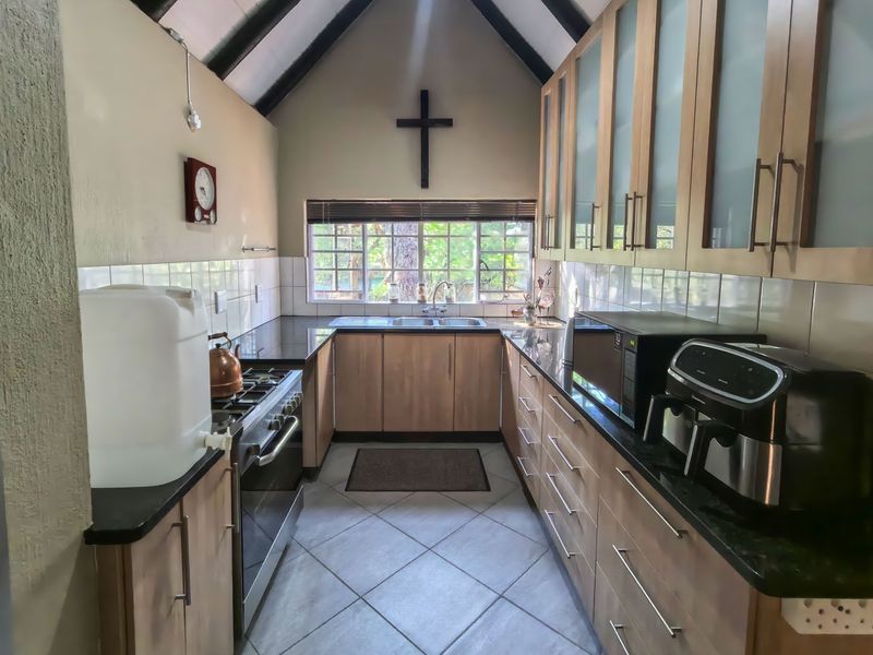 A functional kitchen featuring wood-finish cabinetry, granite countertops, a gas stove, and a distinctive vaulted ceiling with exposed beams.