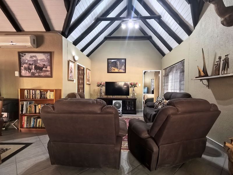 Spacious living room featuring a high vaulted ceiling with exposed timber beams, tiled flooring, and a wall-mounted air conditioning unit.