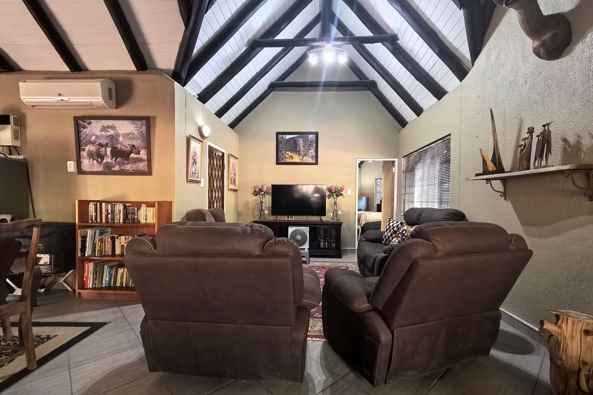Spacious living room featuring a high vaulted ceiling with exposed timber beams, tiled flooring, and a wall-mounted air conditioning unit.