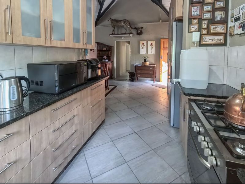 A functional kitchen featuring light wood cabinetry, granite countertops, a gas hob, and tiled flooring, leading into an open-plan living area with vaulted ceilings.