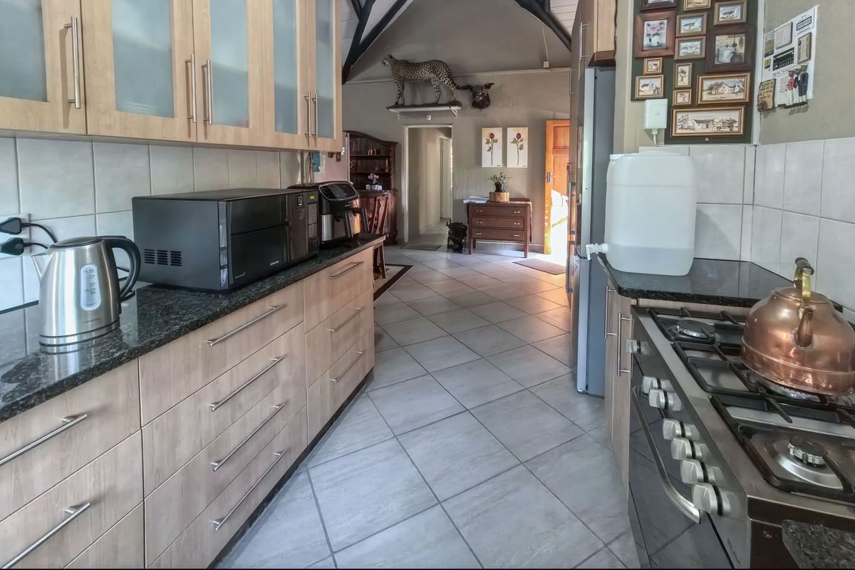A functional kitchen featuring light wood cabinetry, granite countertops, a gas hob, and tiled flooring, leading into an open-plan living area with vaulted ceilings.